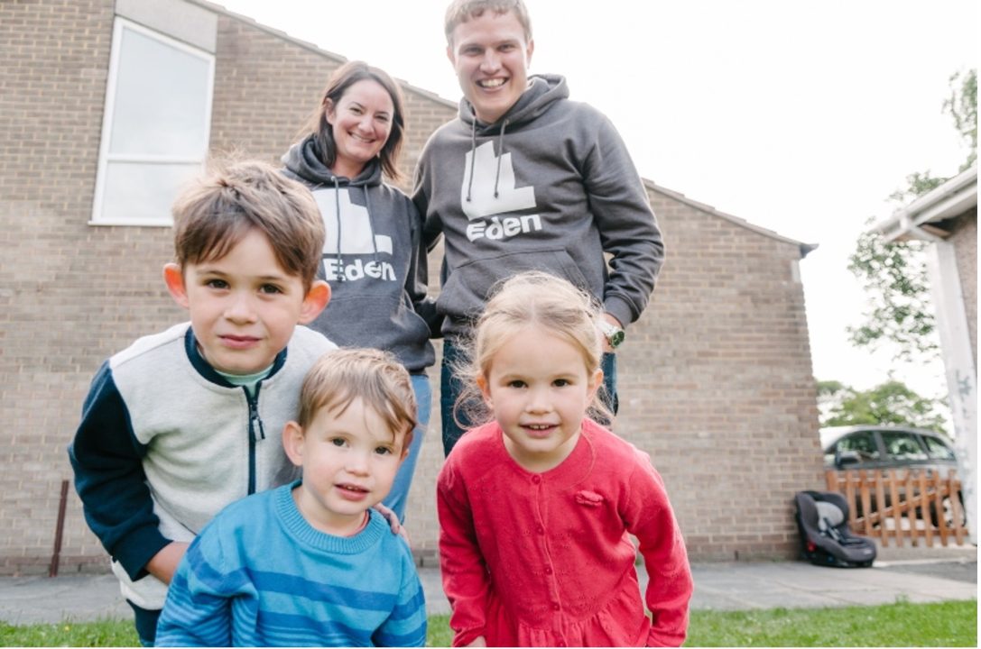 A family with 3 young children stand and smile